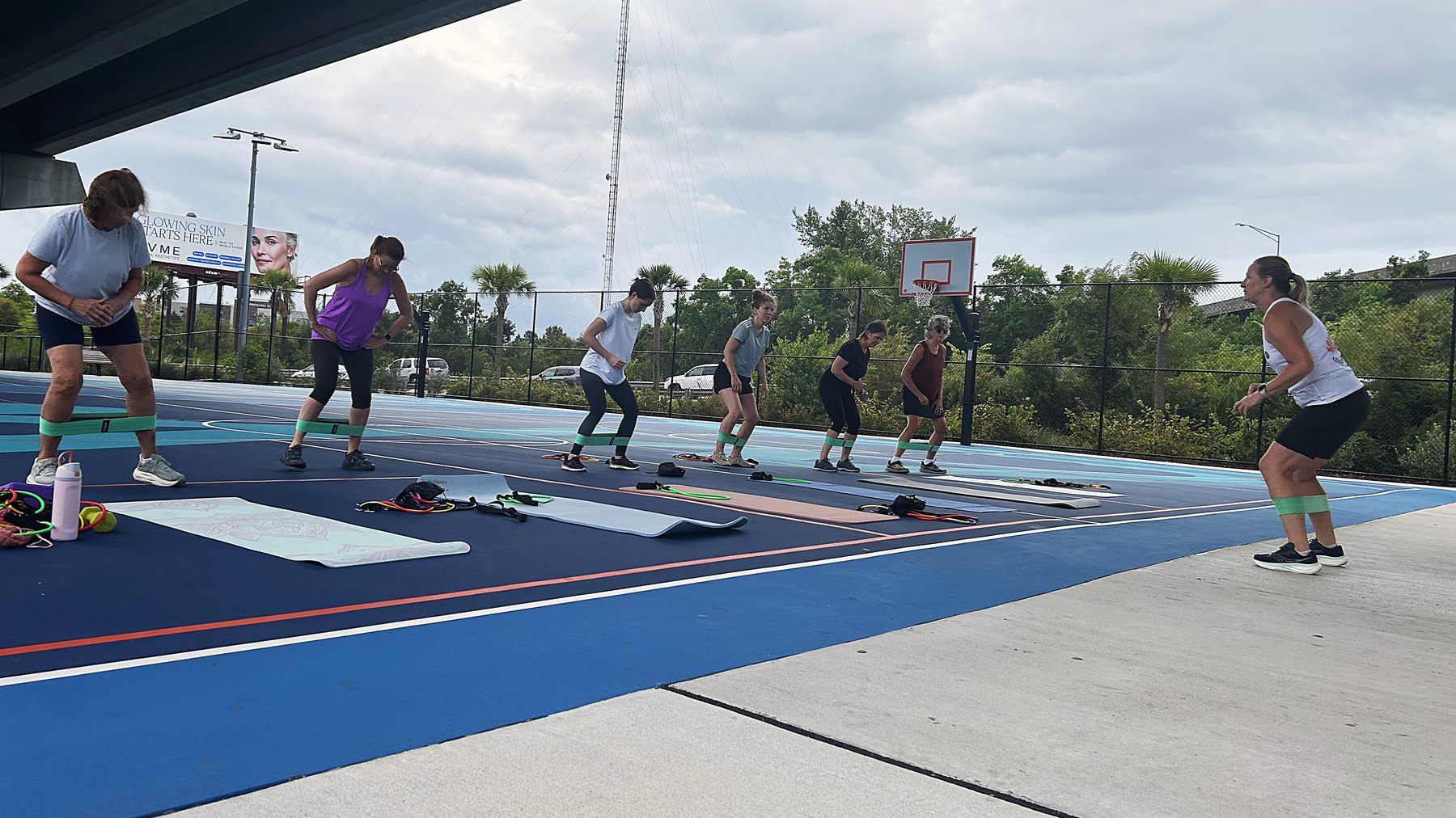 Kim leading a Wednesday class on the courts under the Ravenel Bridge, the group hinged forward with resistance bands around their ankles