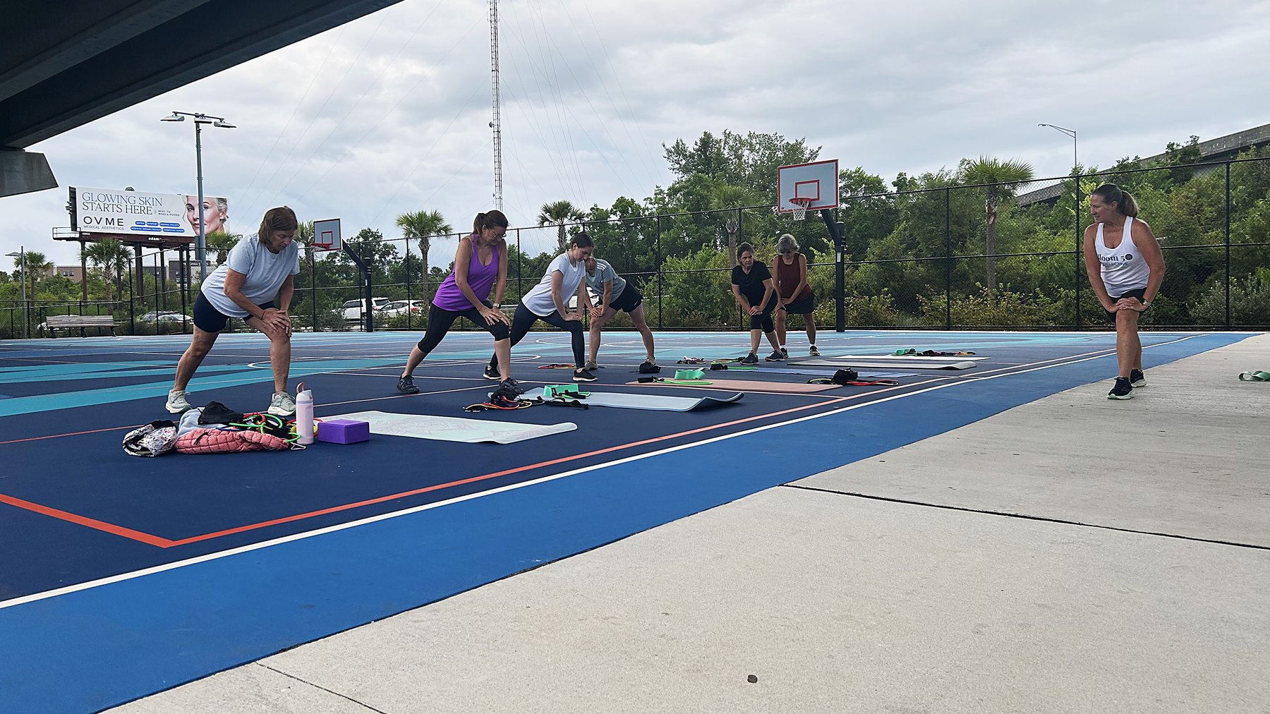 Kim leading the Wednesday warm-up, the group in a wide stance side stretch on the courts under the Ravenel Bridge