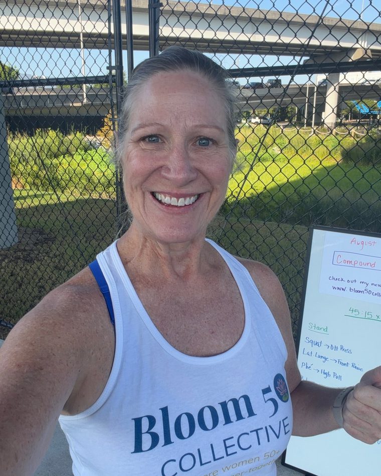 Kim Farrell, founder of Bloom50 Collective, in a Bloom50 tank top beside her workout whiteboard